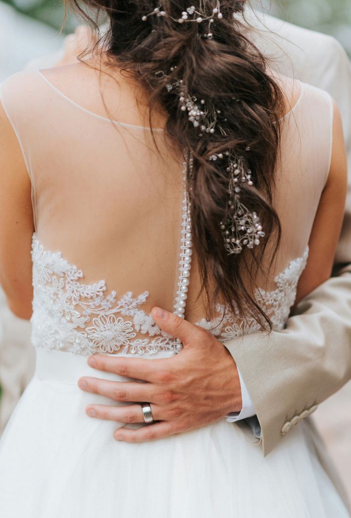 Die Hand des Bräutigams liegt auf der Taille der Braut und zeigt Hochzeitskleidung und Ringe.