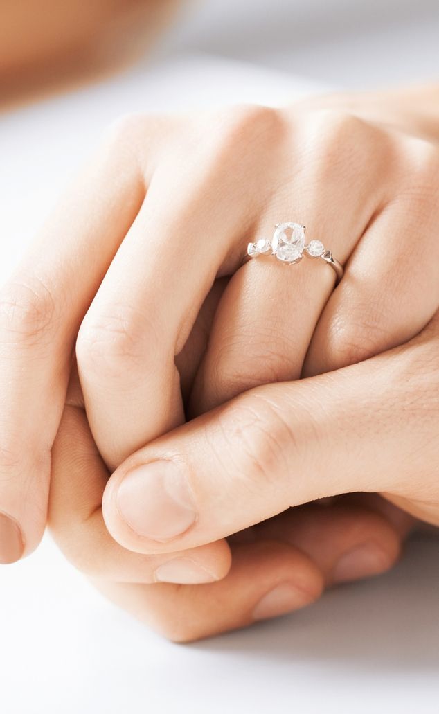 Nahaufnahme von Händen, die einen Verlobungsring mit einem großen Diamanten in der Mitte umklammern.